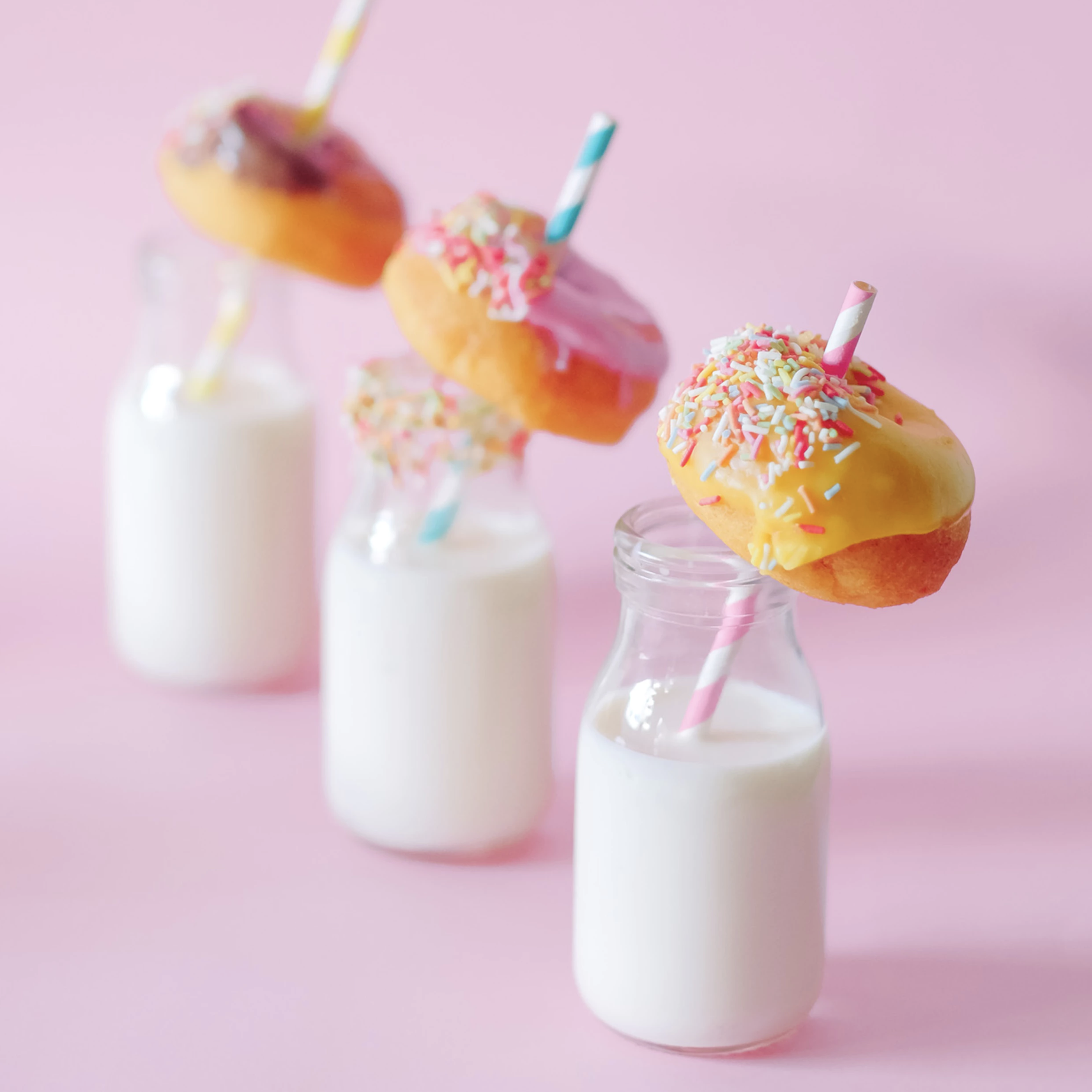 Three glasses of milk with straws holding up donuts in each glass.